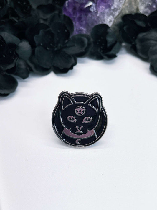 Pictured is an enamel pin of a black cat with a pentagram on its forehead.