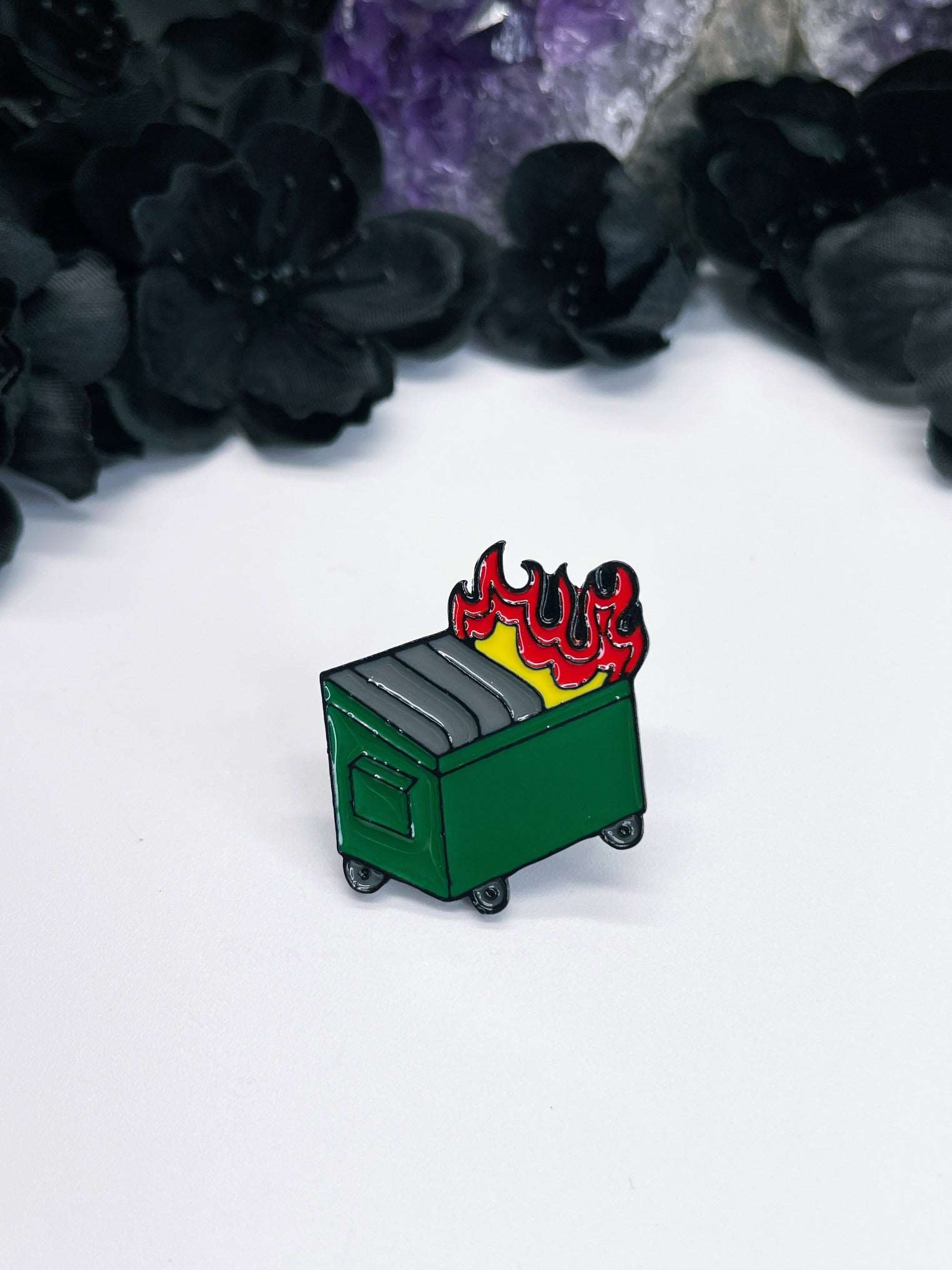 Pictured is an enamel pin of a dumpster fire.