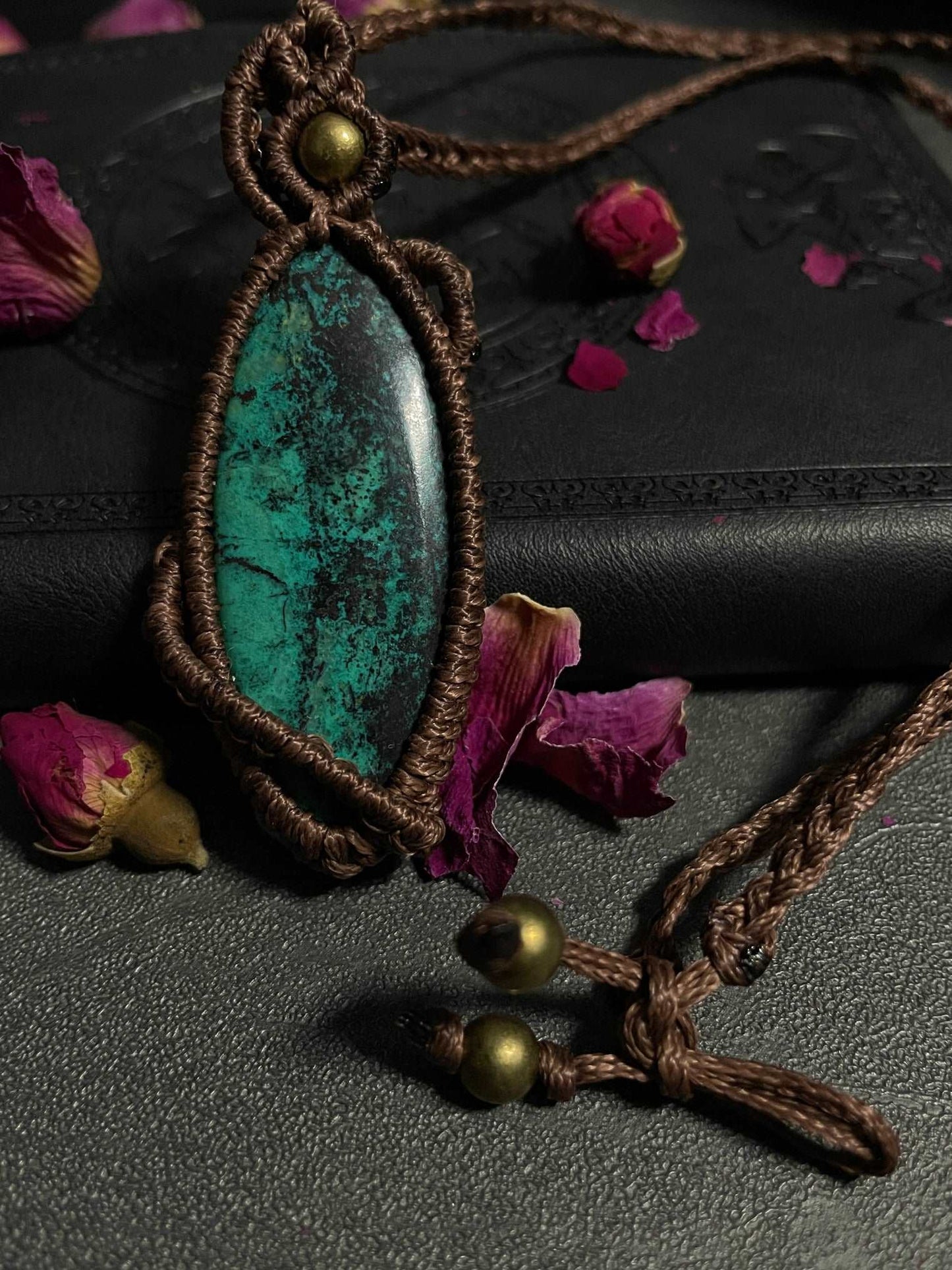Pictured is a chrysocolla cabochon wrapped in macrame thread. A gothic book and flowers are nearby.