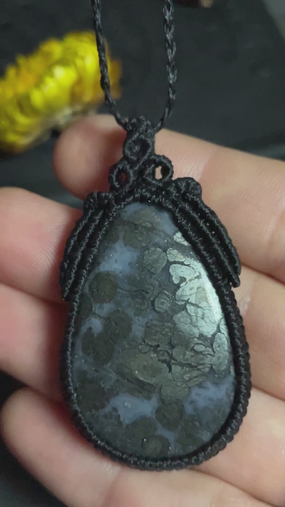 Pictured is a marcasite in agate cabochon wrapped in macrame thread. A gothic book and flowers are nearby.