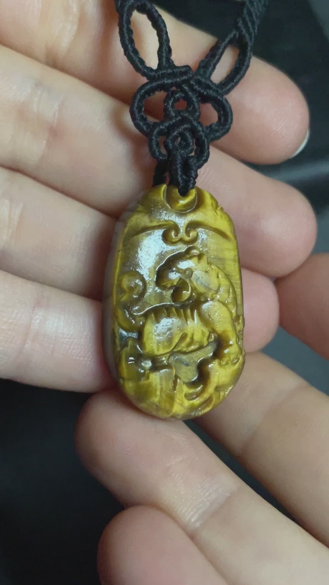 A picture of a tiger pendant carved out of tiger's eye stone. The pendant is on an intricate black macrame necklace.