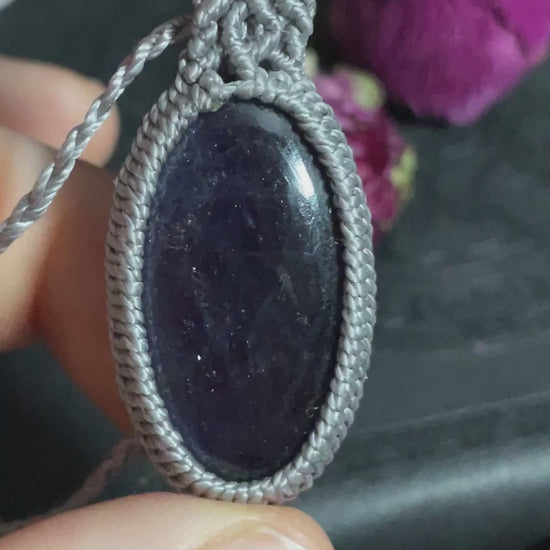 Pictured is an iolite cabochon wrapped in macrame thread. A gothic book and flowers are nearby.