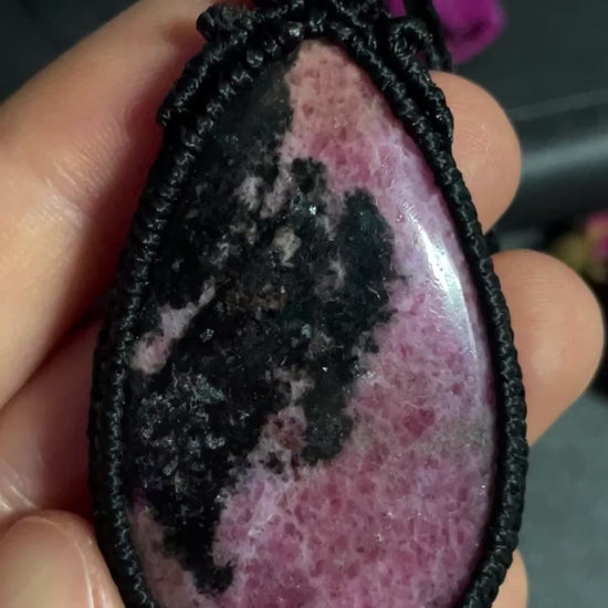 Pictured is a rhodonite cabochon wrapped in macrame thread. A gothic book and flowers are nearby.