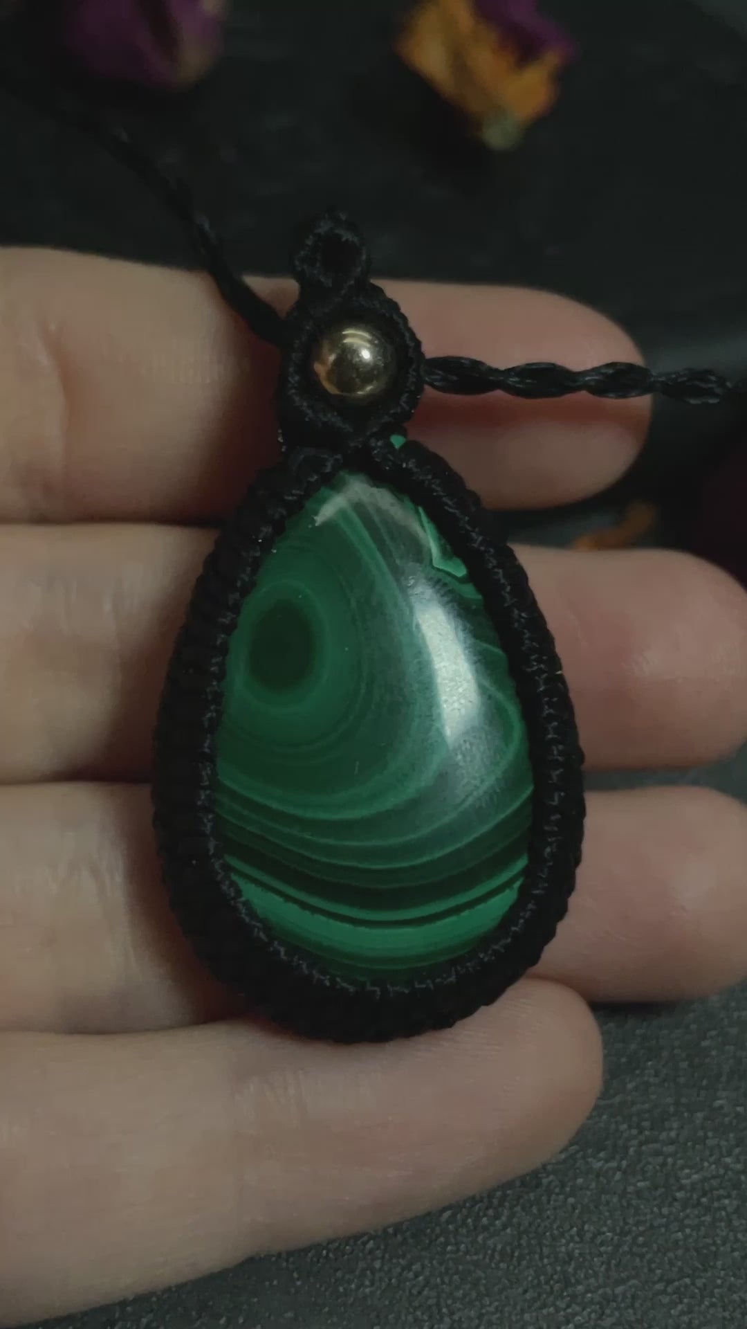 Pictured is a malachite cabochon wrapped in macrame thread. A gothic book and flowers are nearby.