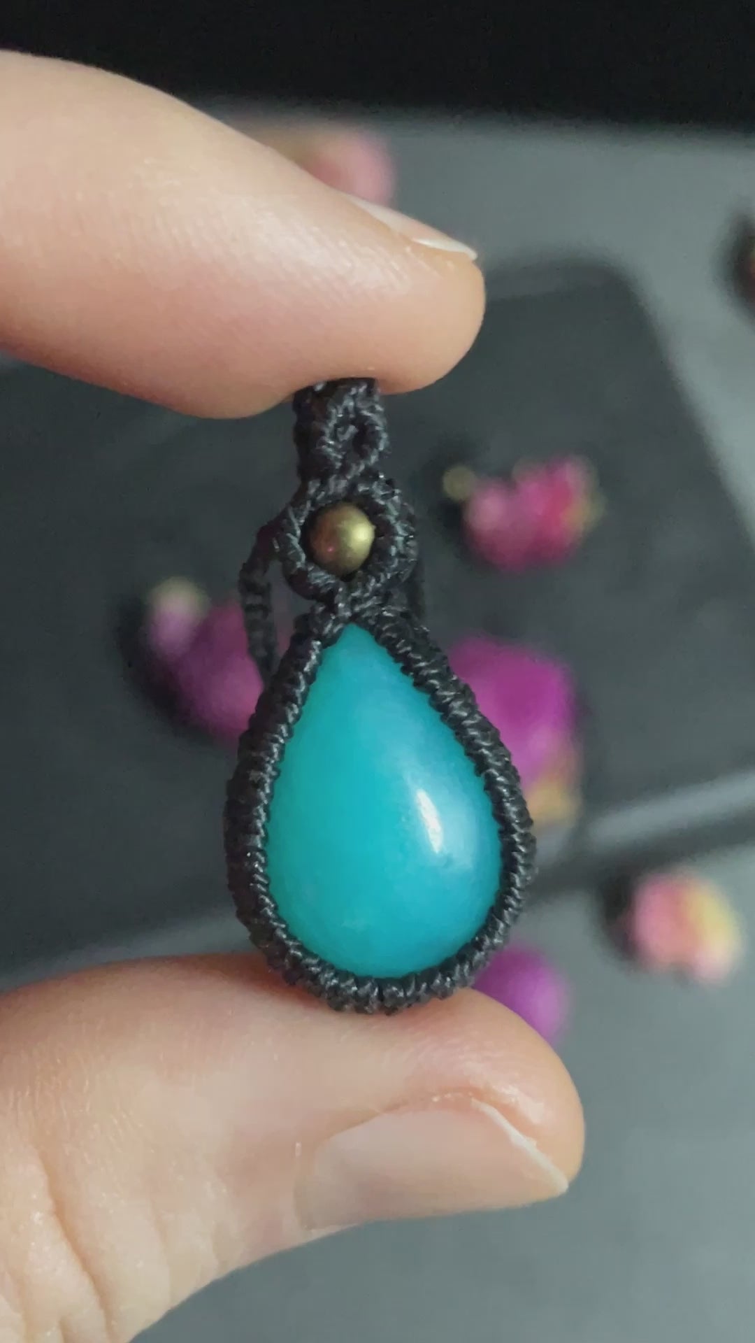 Pictured is a blue mountain jade cabochon wrapped in macrame thread. A gothic book and flowers are nearby.