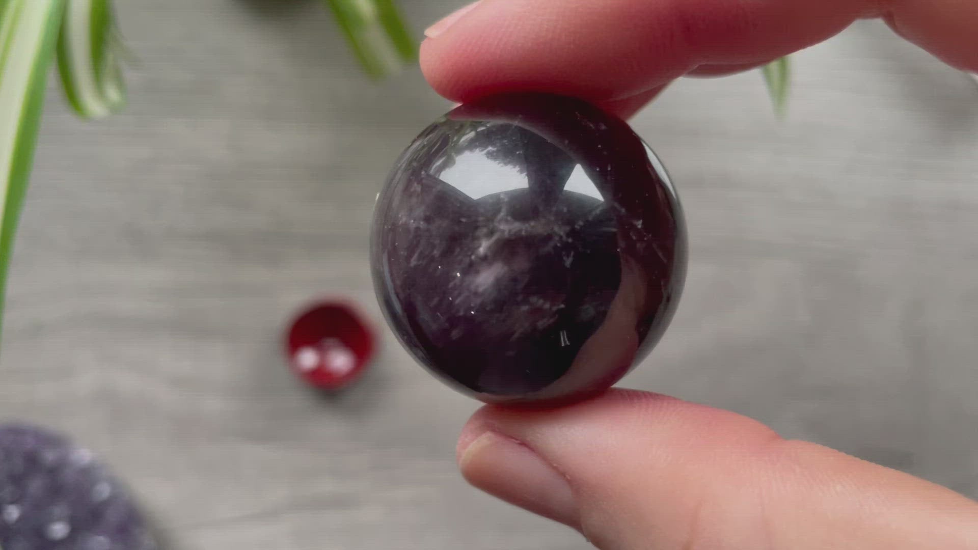 A polished sphere of amethyst is shown in the image. The crystal is a purple color and has a smooth, shiny surface.