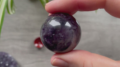 A polished sphere of amethyst is shown in the image. The crystal is a purple color and has a smooth, shiny surface.
