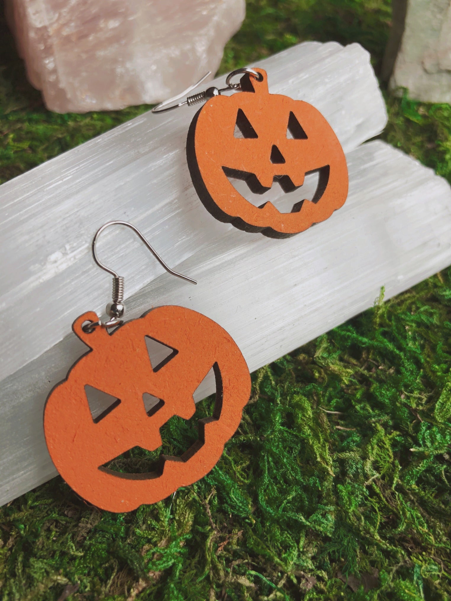 Pictured is a pair of earrings featuring orange pumpkins / jack-o-lanterns. They are made of wood. 