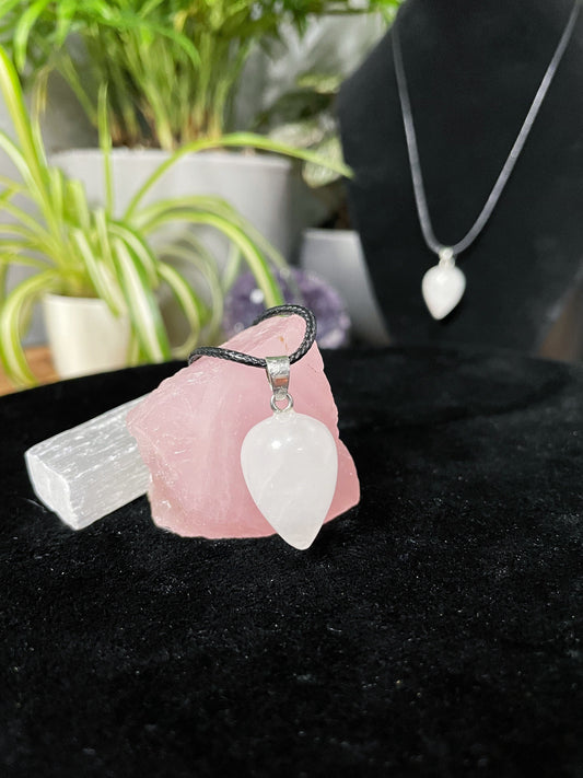 An image of a white quartz turnip shaped pendant on a necklace. It sits atop some selenite chunks and a black velvet surface.