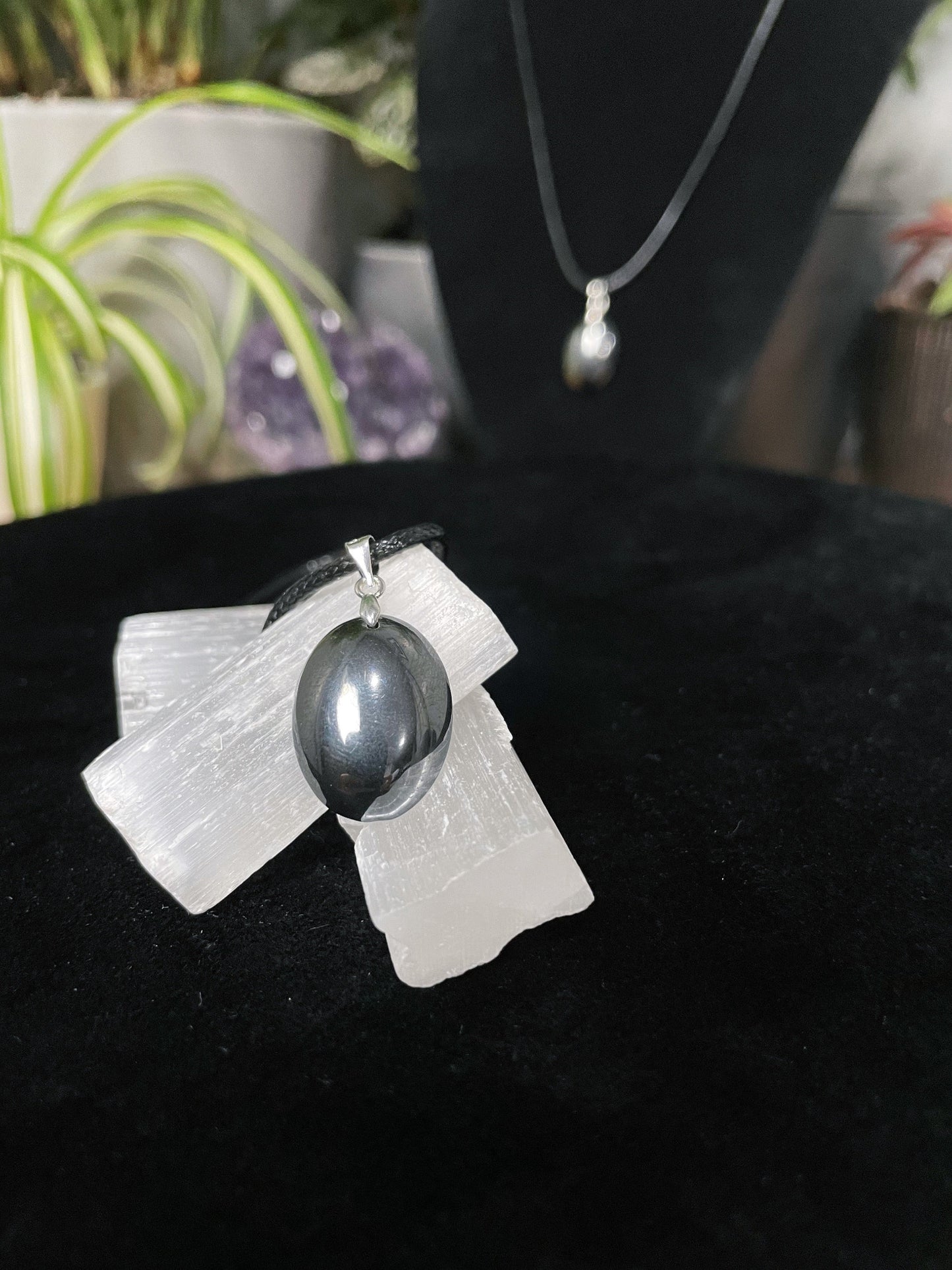 An image of a terahertz oval shaped pendant on a necklace. It sits atop some selenite chunks and a black velvet surface.