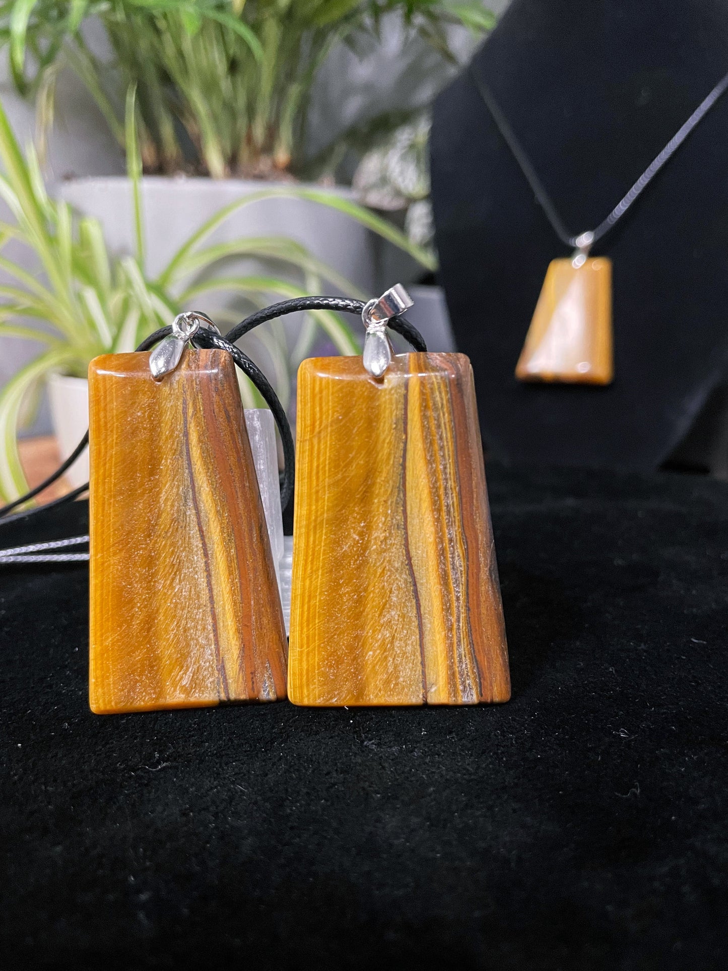 An image of a matching pair of yellow tiger's eye rectangular shaped pendants on necklaces. They sit atop some selenite chunks and a black velvet surface.