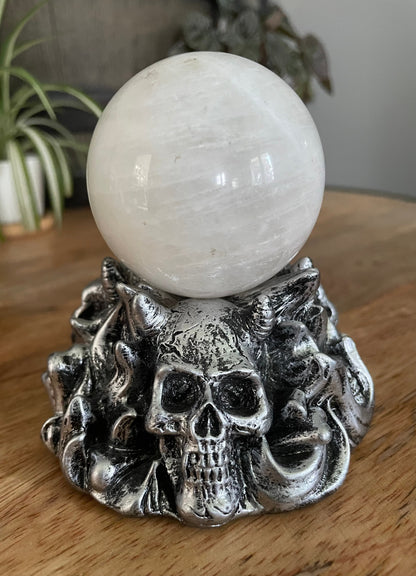 Pictured is a silver resin sphere holder with various demon skulls on it.
