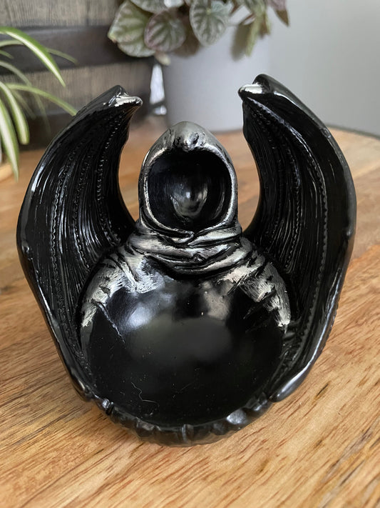 Pictured is a sphere stand in the shape of a hooded figure with dragon wings.