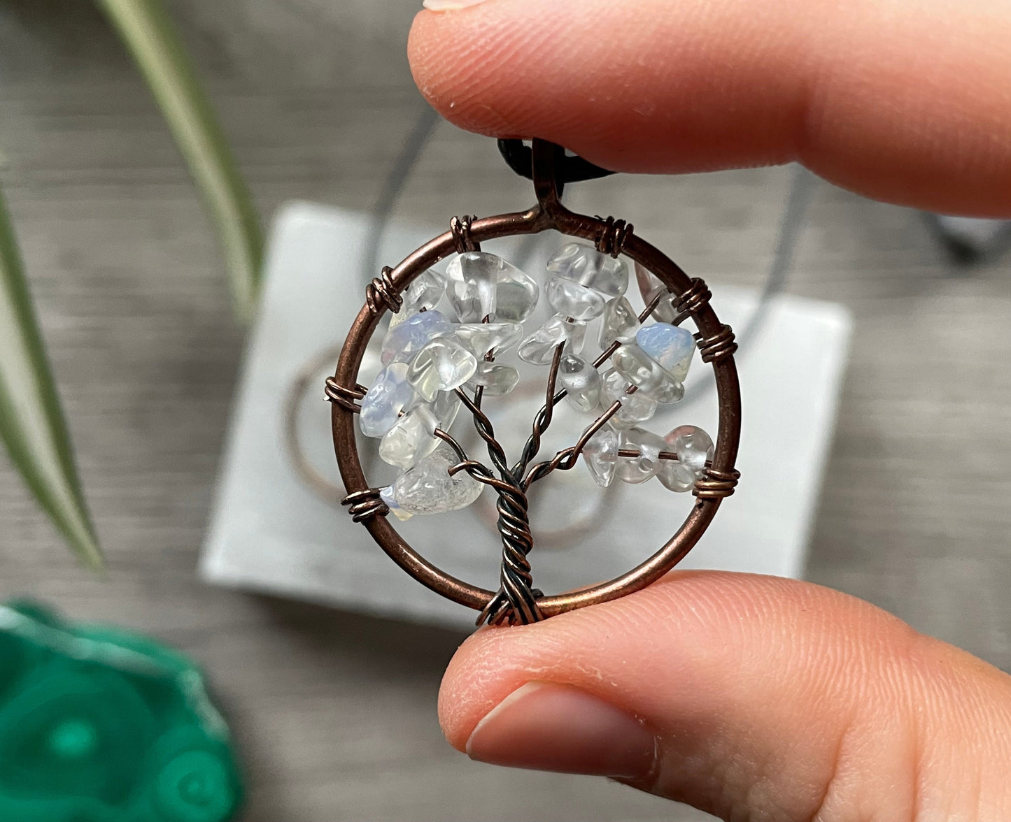 An image of a necklace featuring a wire-wrapped pendant. The wire is in the shape of a tree and the leaves on the tree are polished chips of opalite.