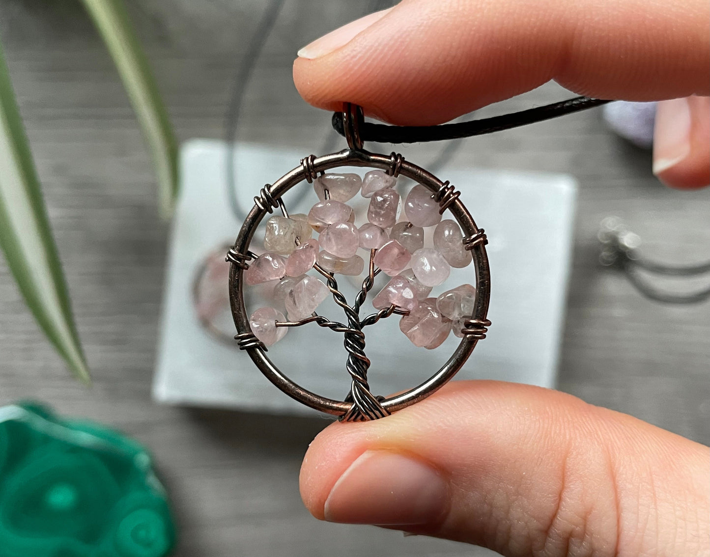 An image of a necklace featuring a wire-wrapped pendant. The wire is in the shape of a tree and the leaves on the tree are polished chips of rose quartz.