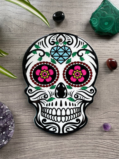 Pictured is a ceramic trivet in the shape of a sugar skull with bright colours.
