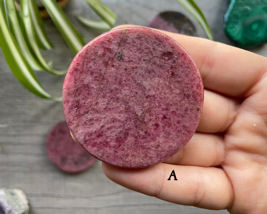 Pictured is a rhodonite crystal coin.