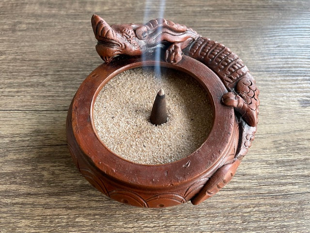 Pictured is a brown incense sand holder in the shape of a bowl with a dragon laying on the side of the bowl.