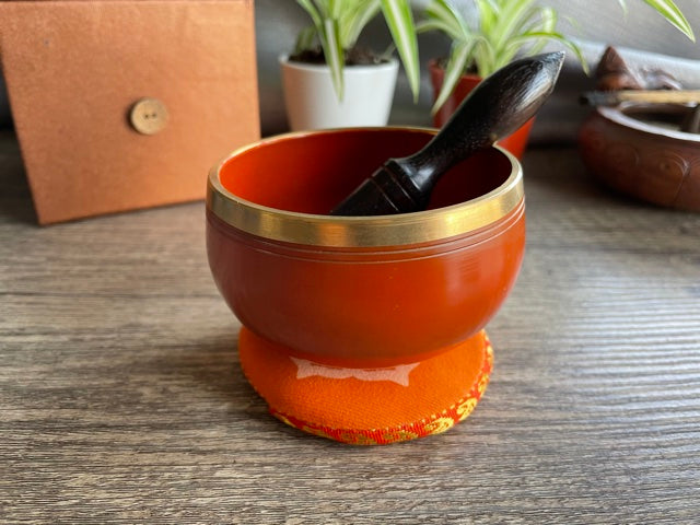 Pictured is a small metal singing bowl with a pillow and a wood gong mallet.