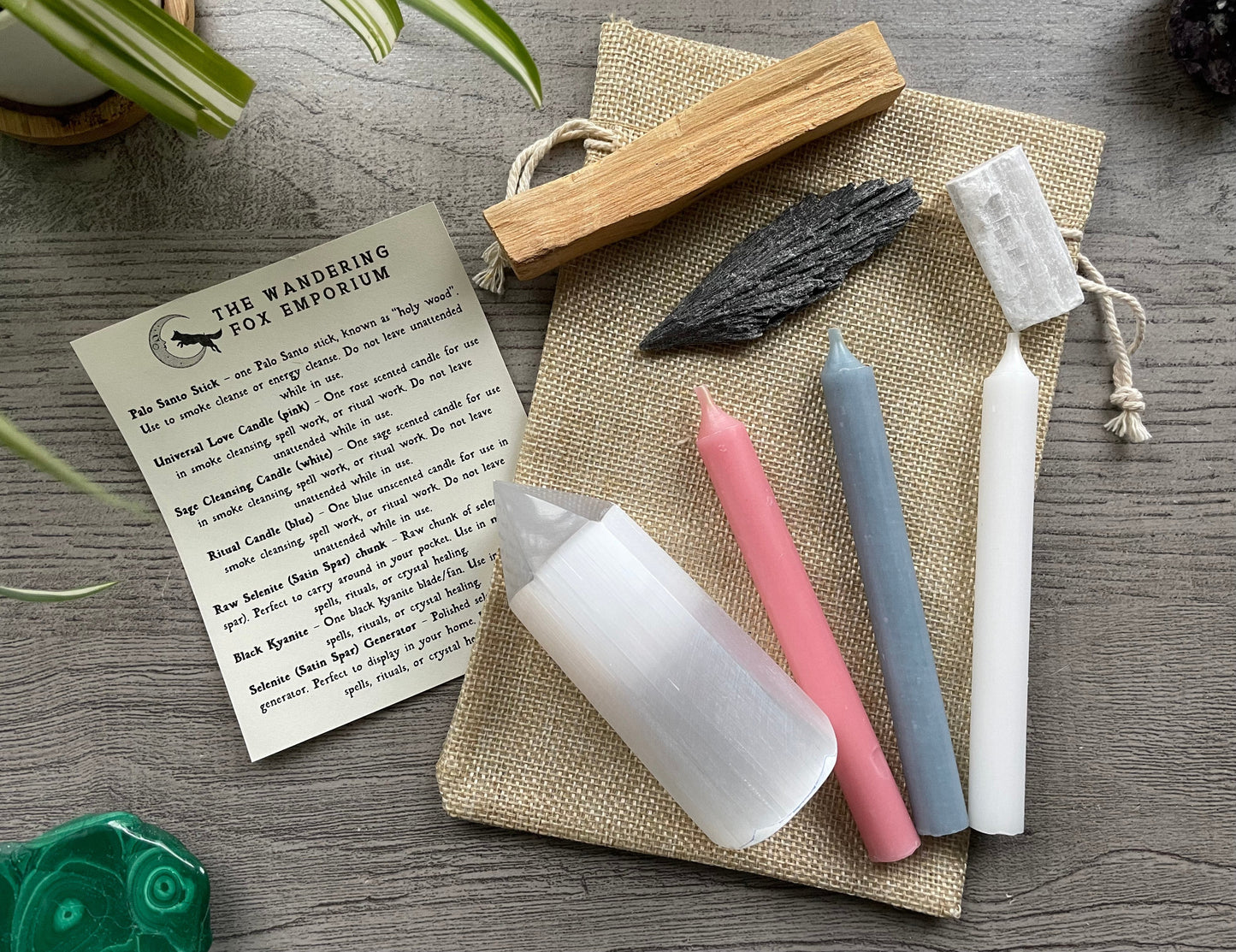 Pictured is a protection and cleansing starter set with candles, selenite, kyanite, palo alto, and a piece of paper explaining how to use the items next to it.