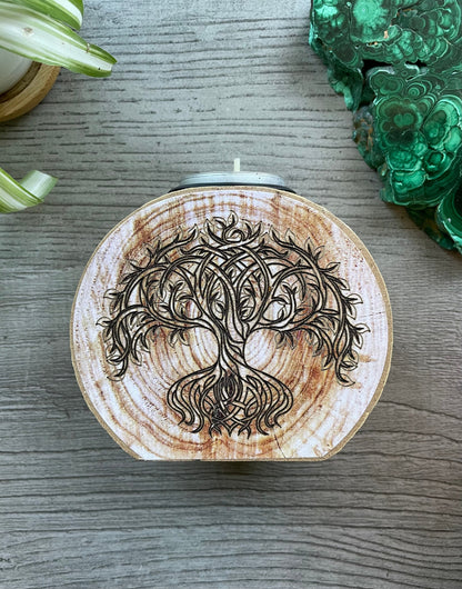 Pictured is a wood tree slice candle holder with a tree of life envraged on it.