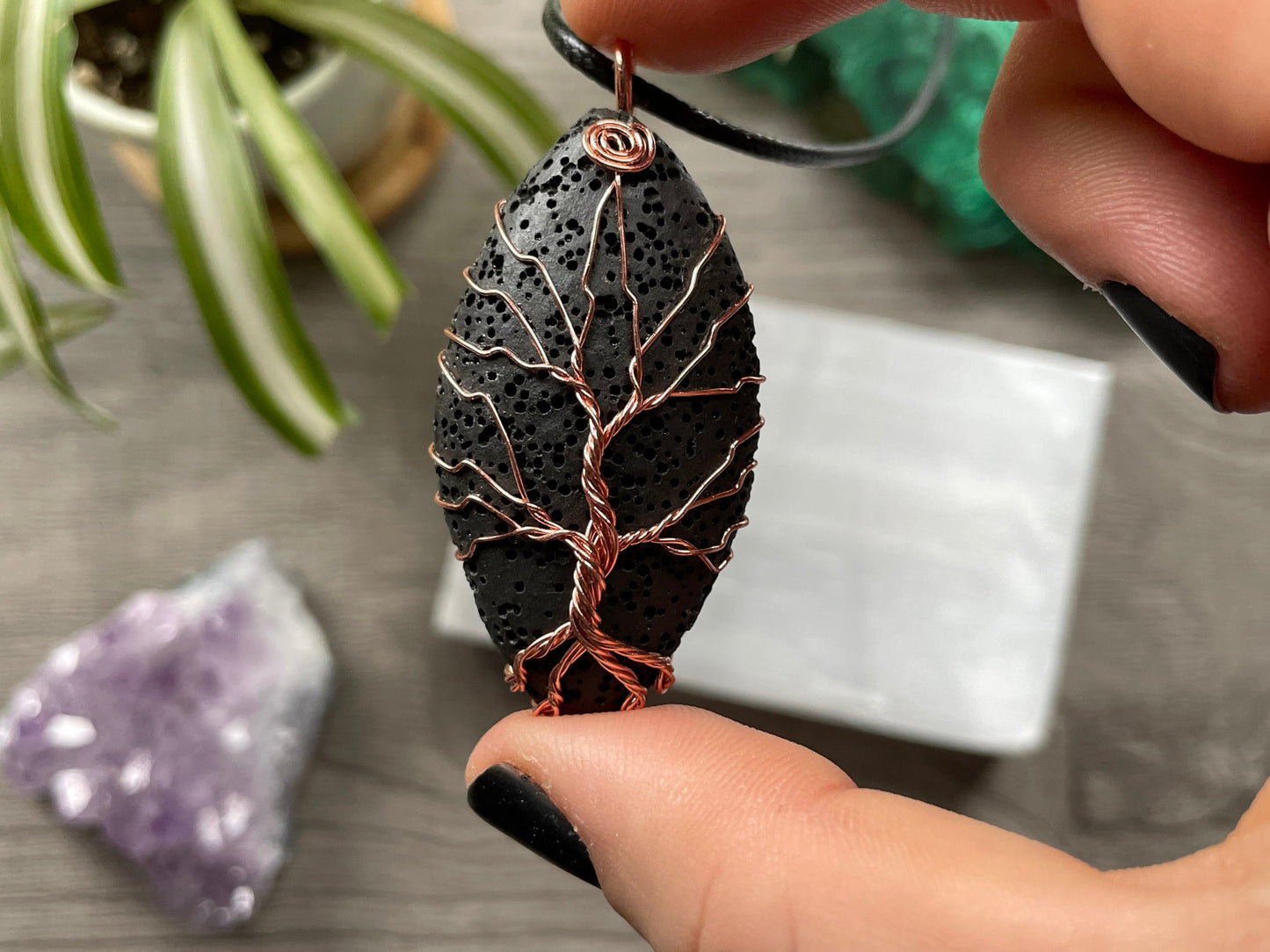 An image of a necklace featuring a wire-wrapped pendant. The wire is in the shape of a tree and it is wrapped around a lava stone.