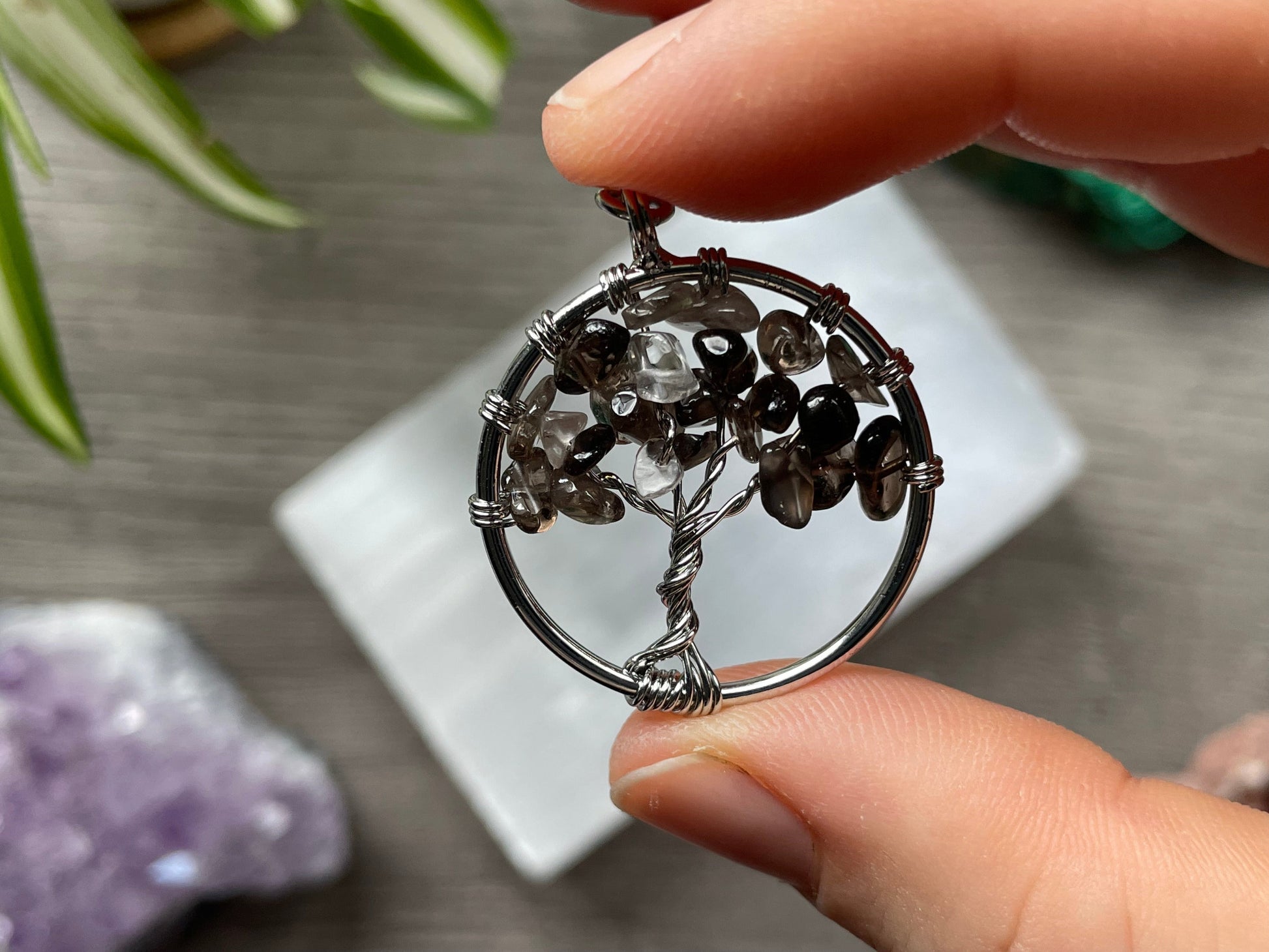 A tree of life with smoky quartz crystals as the leaves on the tree is in the image. The keychain has a number of small multi-coloured beads to represent the chakras on the chain. The keychain sits atop a slab of selenite. Malachite, pink amethyst, and amethyst are nearby.