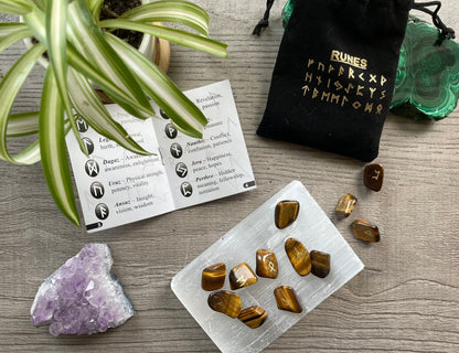 Pictured is a rune set made of tiger's eye tumbled stones. A black velvet bag and instructions sit nearby,