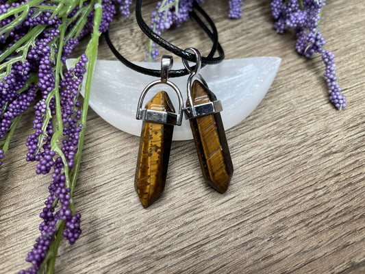An image of yellow tiger's eye double-terminated polished crystal necklaces sitting on selenite and surrounded by lavender on a wood surface..