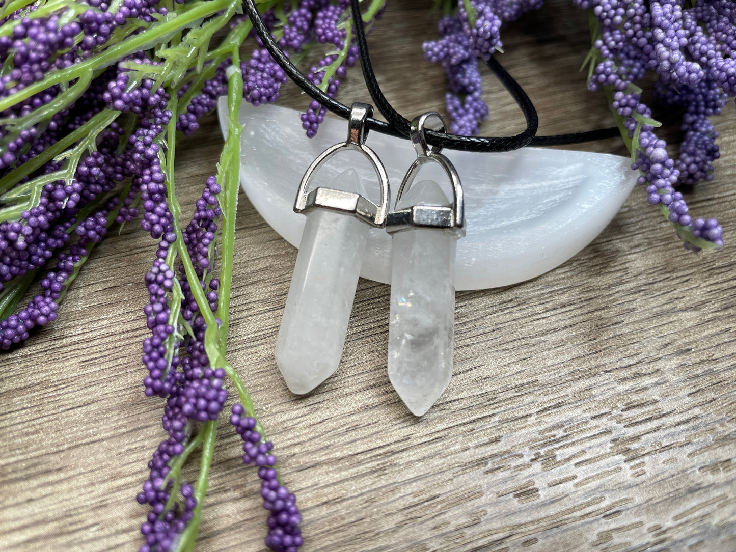 An image of clear quartz double-terminated polished crystal necklaces sitting on selenite and surrounded by lavender on a wood surface..