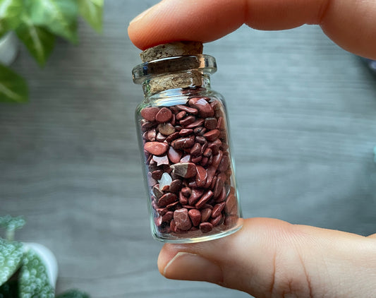 Pictured is a small glass vial with a cork stopper. Inside the jar are red jasper chips.