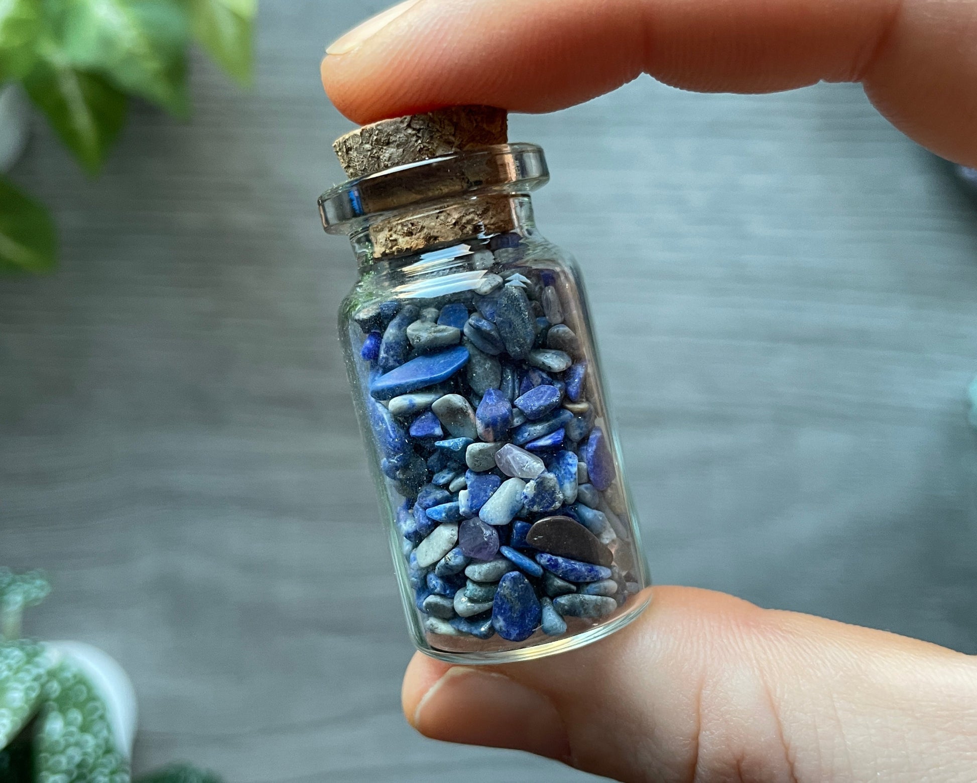 Pictured is a small glass vial with a cork stopper. Inside the jar are lapis lazuli chips.