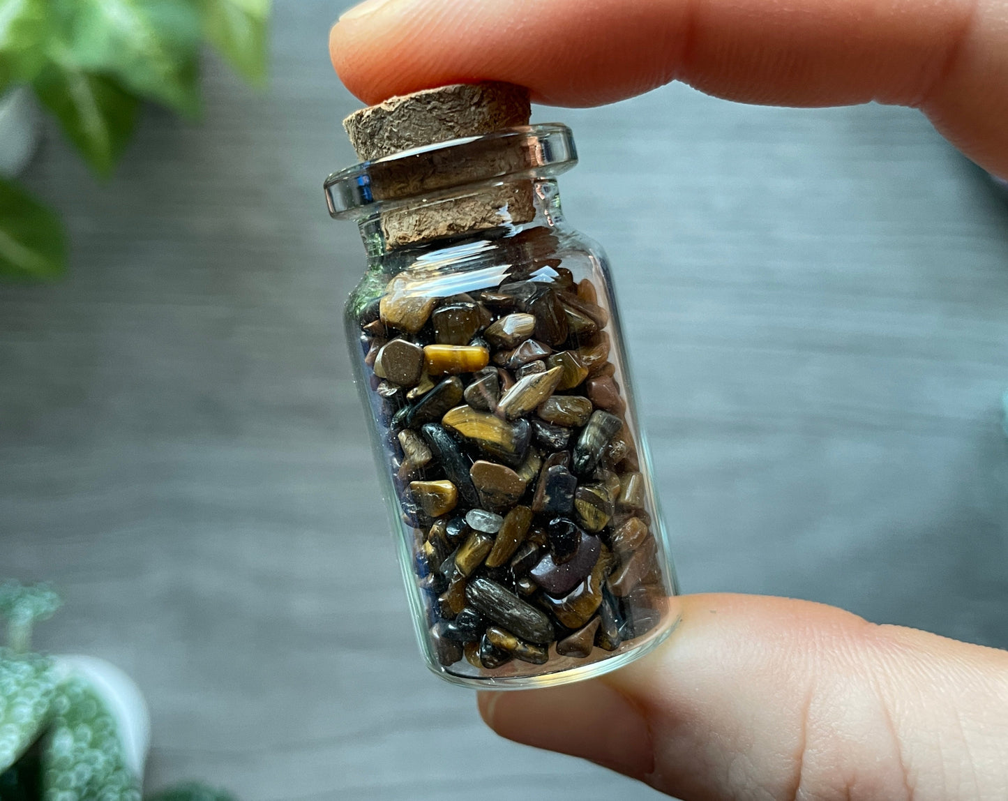 Pictured is a small glass vial with a cork stopper. Inside the jar are tiger's eye chips.
