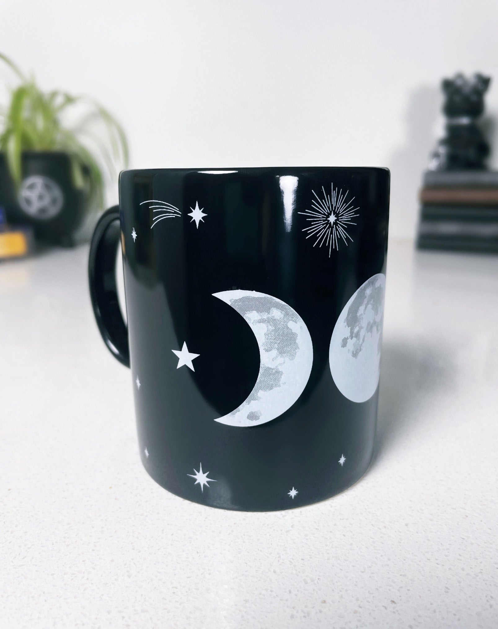 Pictured is a black ceramic mug with a triple moon on it.