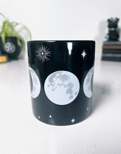 Pictured is a black ceramic mug with a triple moon on it.