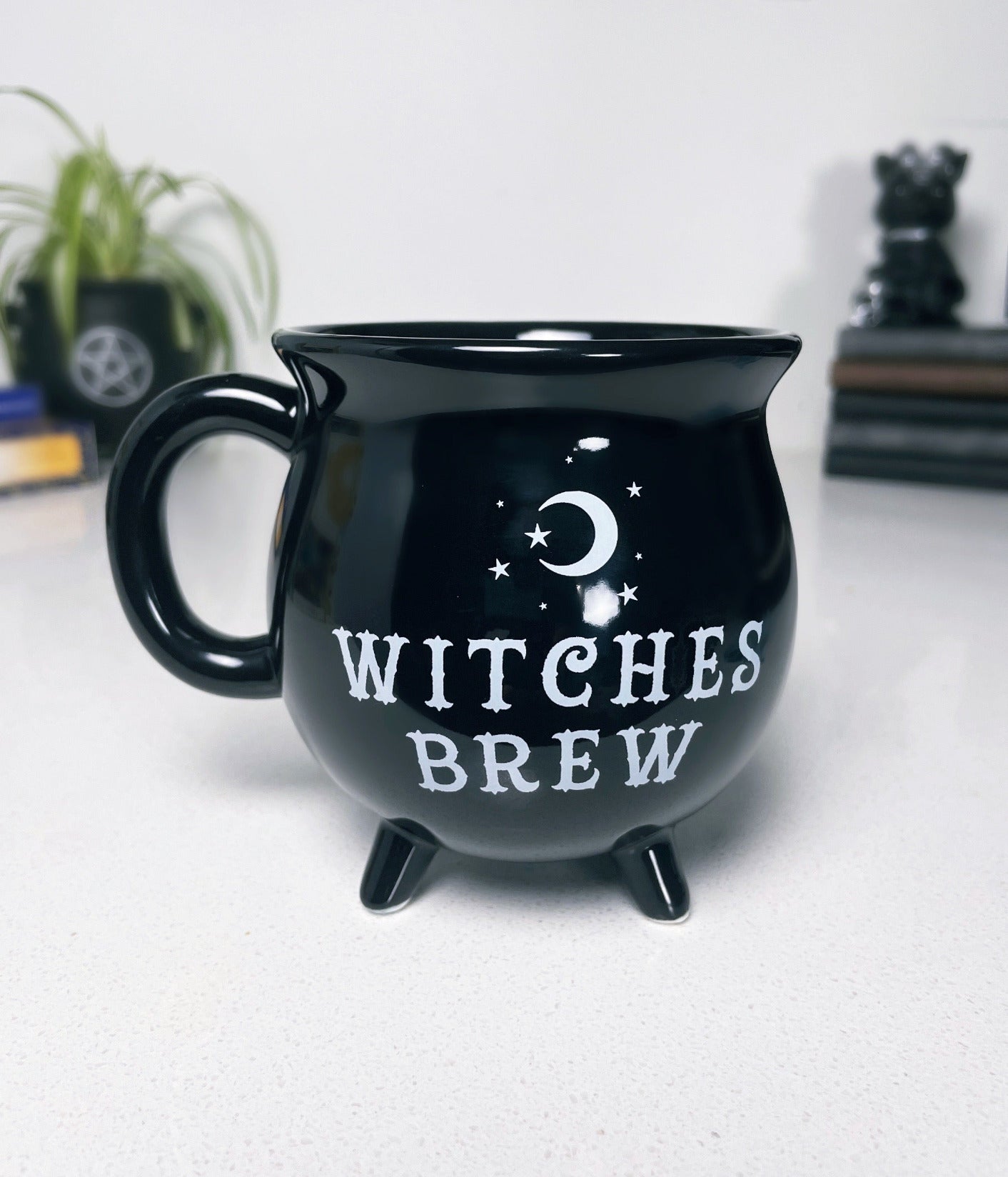 A black ceramic cauldron-shaped mug with a white label that says "Witches Brew" on the side. 