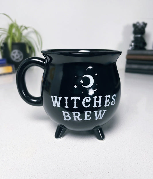 A black ceramic cauldron-shaped mug with a white label that says "Witches Brew" on the side. 