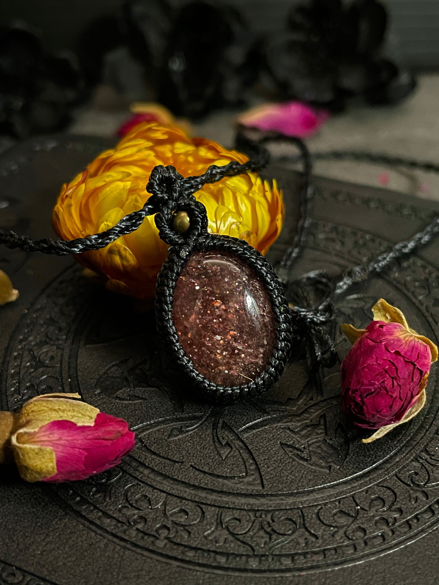 Pictured is a strawberry quartz cabochon wrapped in macrame thread. A gothic book and flowers are nearby.