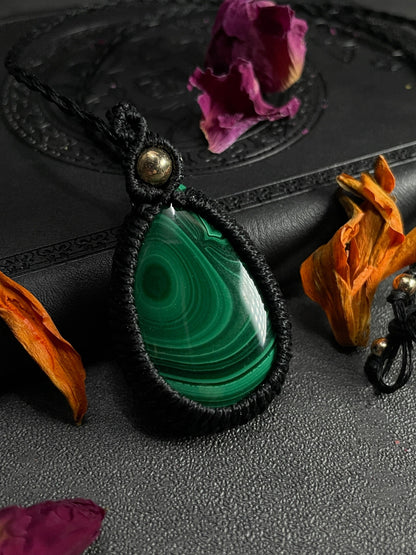 Pictured is a malachite cabochon wrapped in macrame thread. A gothic book and flowers are nearby.