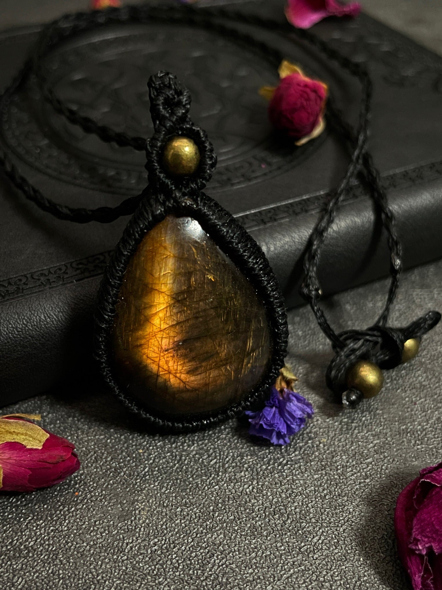 Pictured is a labradorite cabochon wrapped in macrame thread. A gothic book and flowers are nearby.
