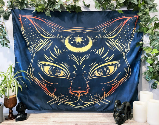 Pictured is a large wall tapestry with a dark blue background and a large cat with a crescent moon on its forehead printed in yellow and orange.