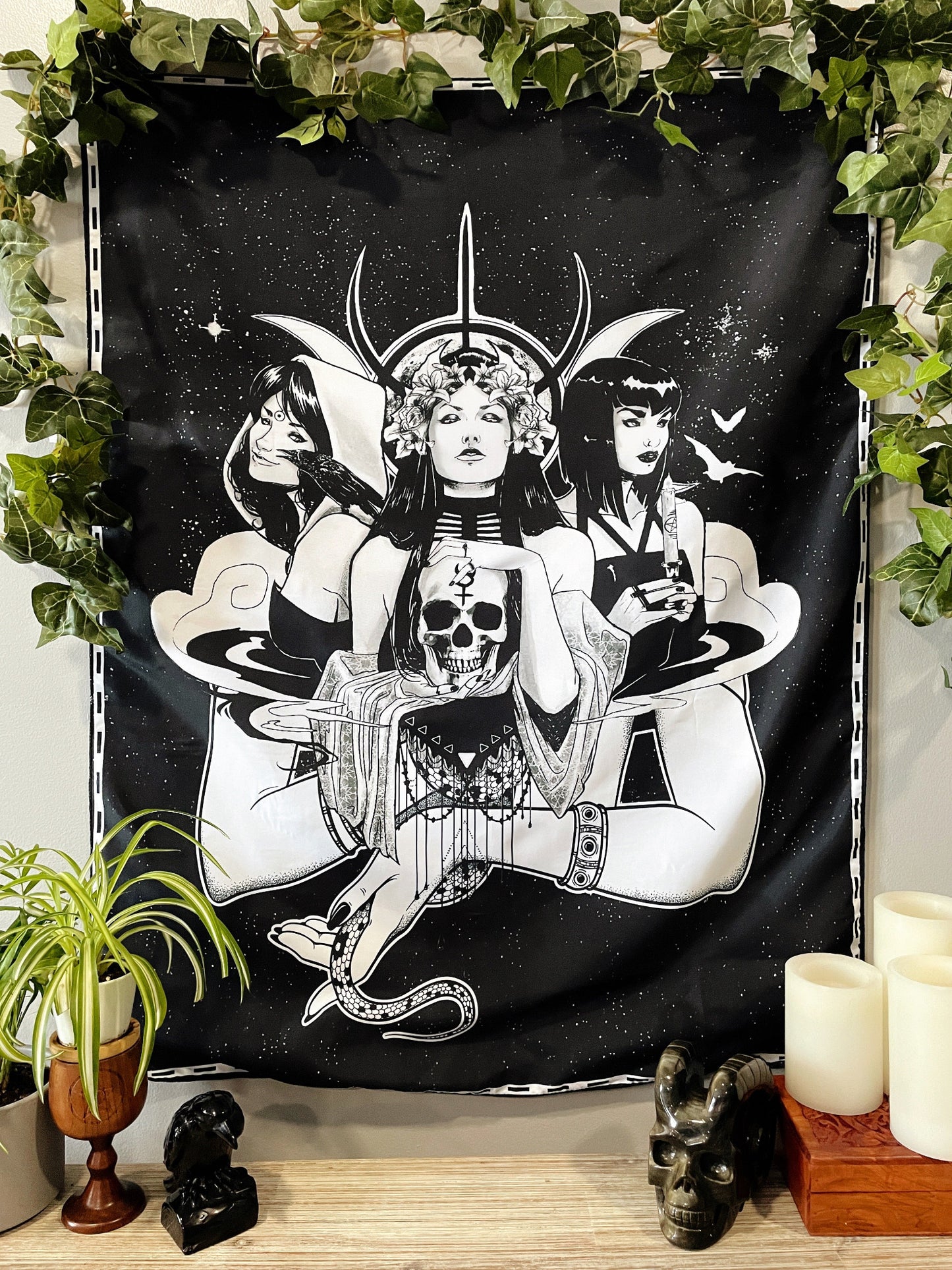 Pictured is a large wall tapestry with a black background and three women representing triple goddesses or Hecate printed in white on it.