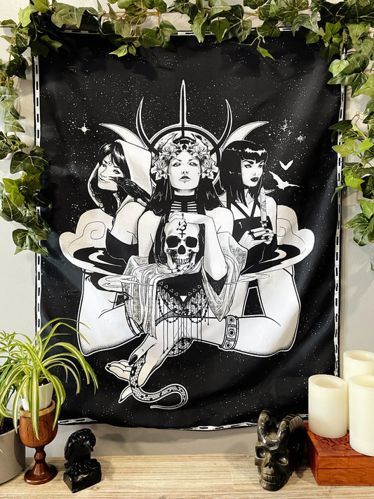 Pictured is a large wall tapestry with a black background and three women representing triple goddesses or Hecate printed in white on it.