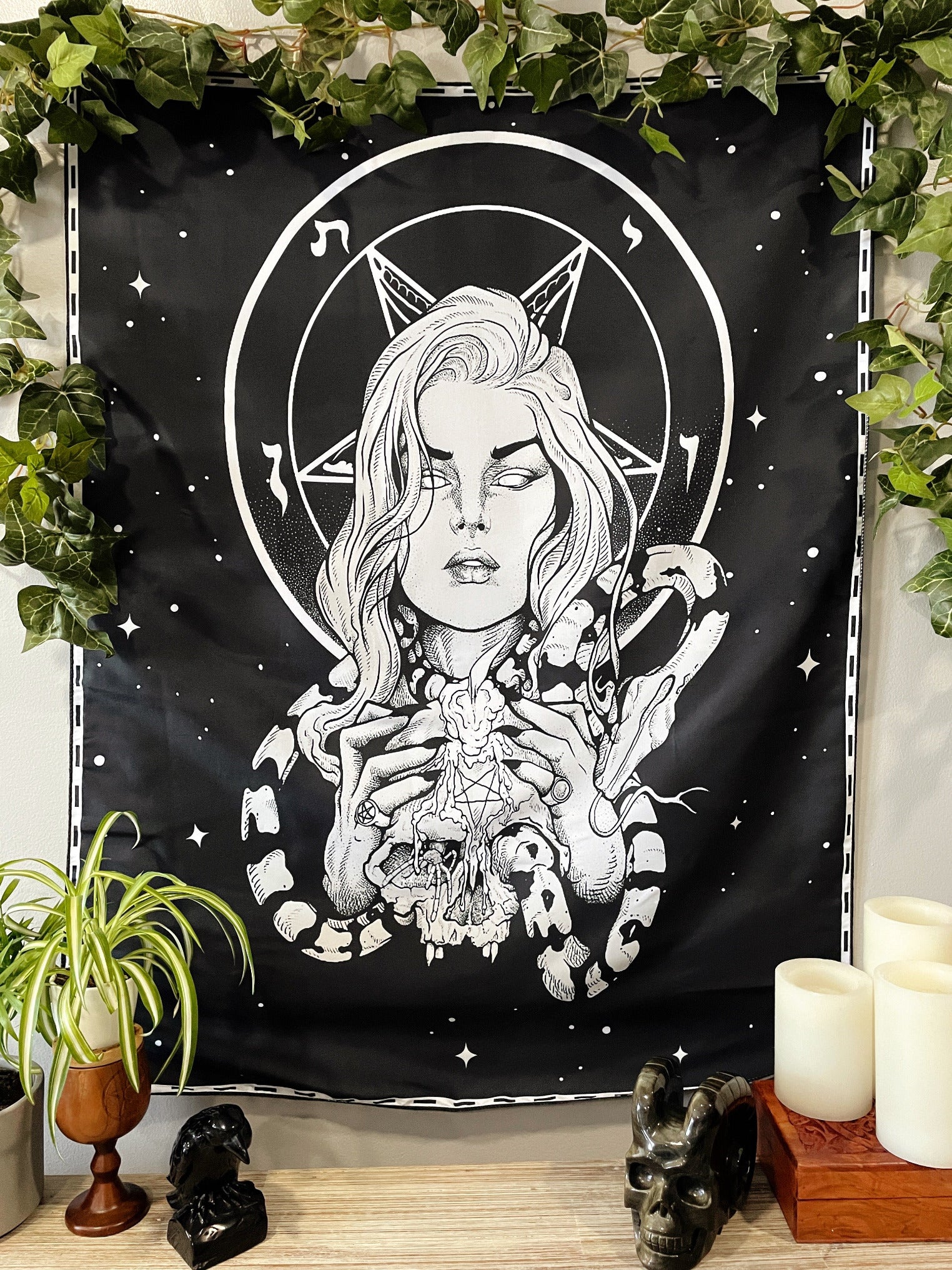 Pictured is a large wall tapestry with a black background and a woman holding a skull with a snake wrapped around it printed in white on it.
