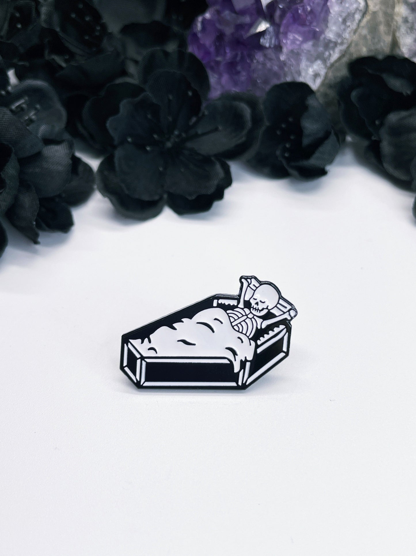 Pictured is an enamel pin of a skeleton sleeping inside a coffin.