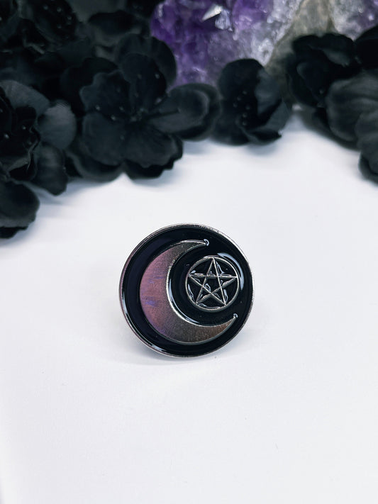Pictured is an enamel pin of a crescent moon and a pentagram.