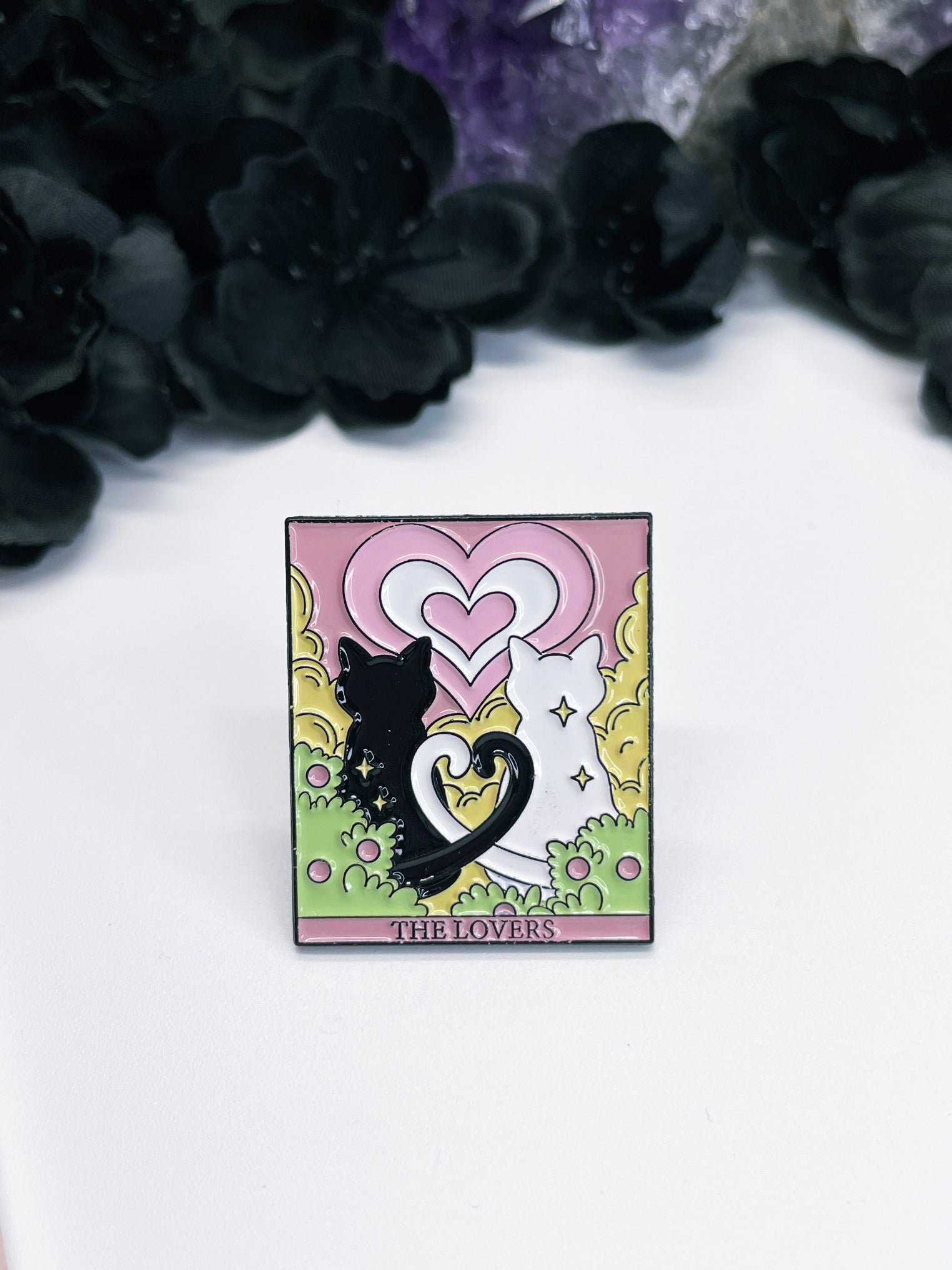  An enamel pin featuring a tarot card with a black cat and a white cat on it, the card is "The Lovers."