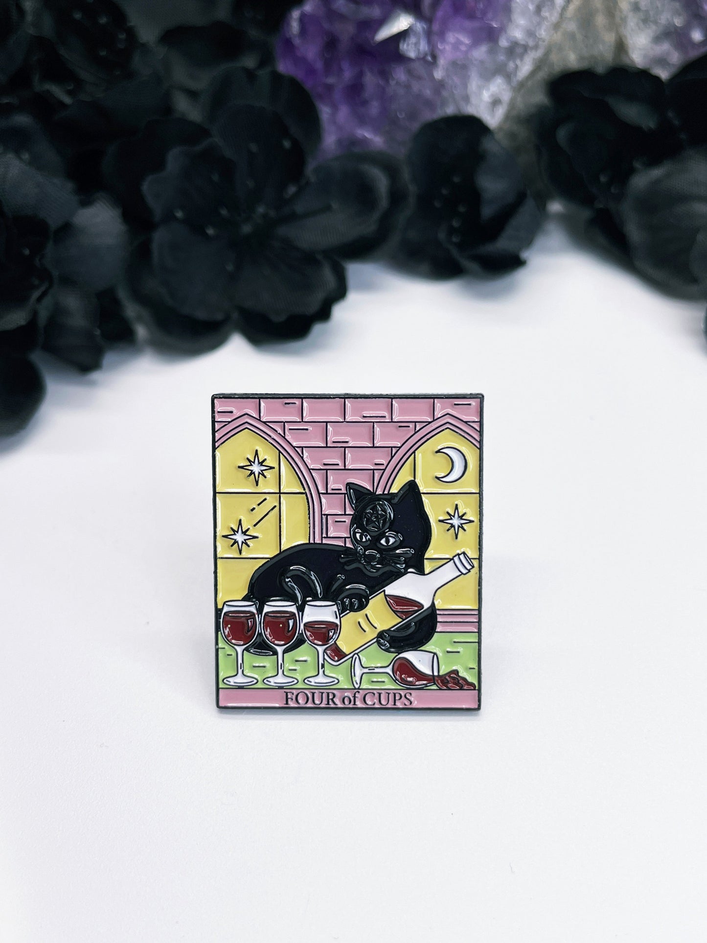 An image of an enamel pin featuring the Tarot card "Four of Cups" with a black cat pouring glasses of wine. The pin is circular with a black border and has one metal fastener on the back. The card features a black cat sitting in front of a table with four cups, pouring wine out.