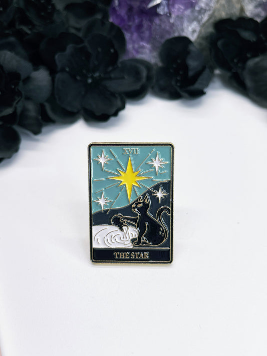  An enamel pin featuring a tarot card with a black cat on it, the card is "The Star."