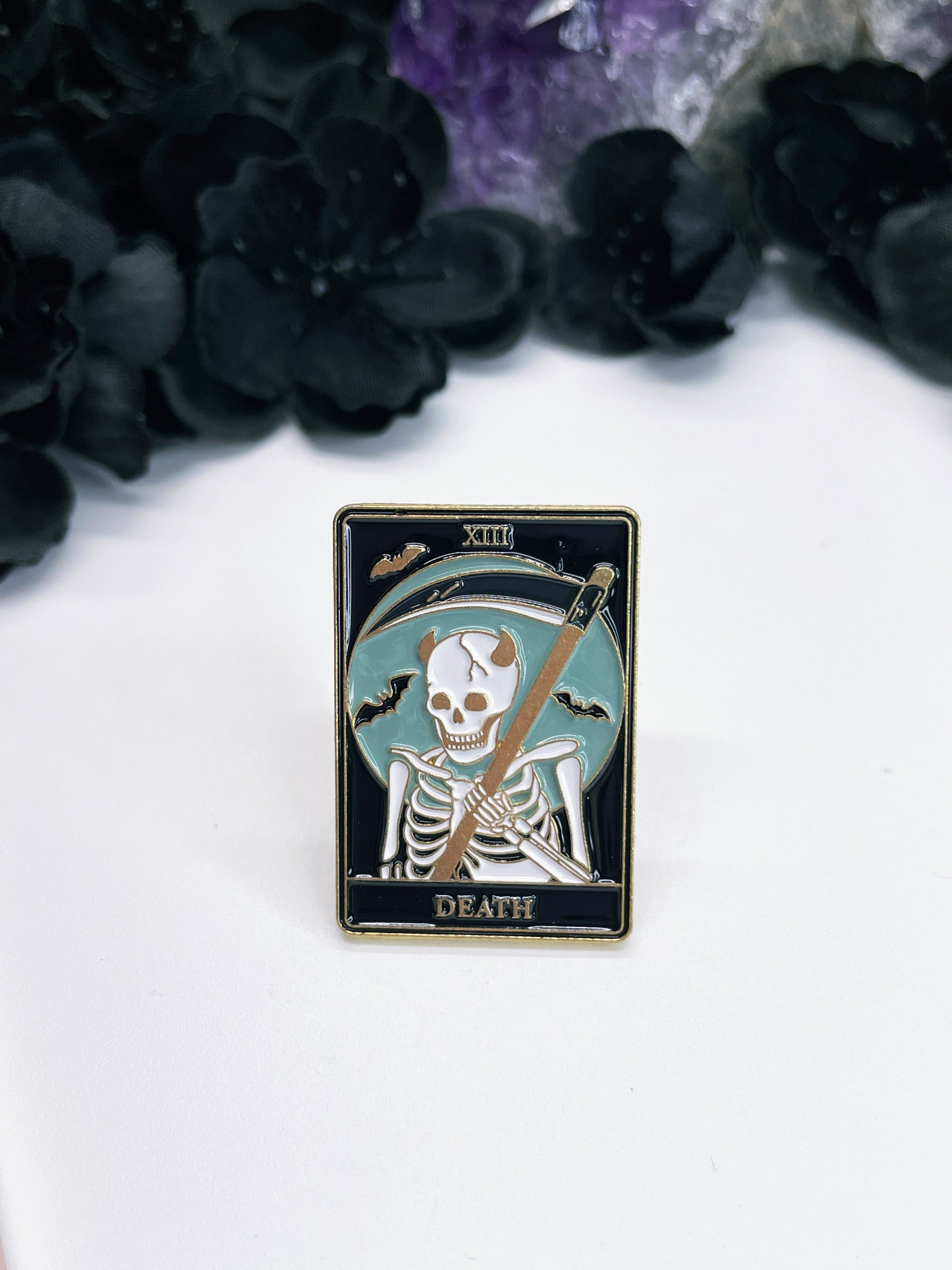 An image of an enamel pin featuring the Tarot card "Death" and a stylized skeleton with a reaper on it.